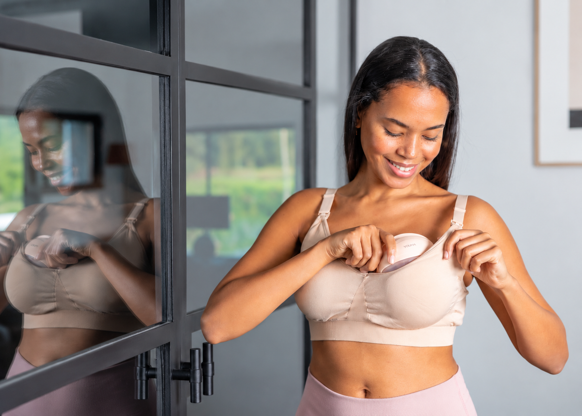 Glimlachende moeder plaatst een Youha handsfree borstkolf in haar voedingsbh. De draadloze borstkolf wordt discreet onder de bh gedragen, zodat ze comfortabel kan kolven.