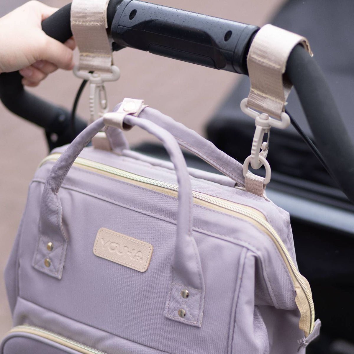 Youha luiertas bevestigd aan een kinderwagen met bevestigingshendel, ideaal voor ouders die onderweg zijn en hun handen vrij willen houden.